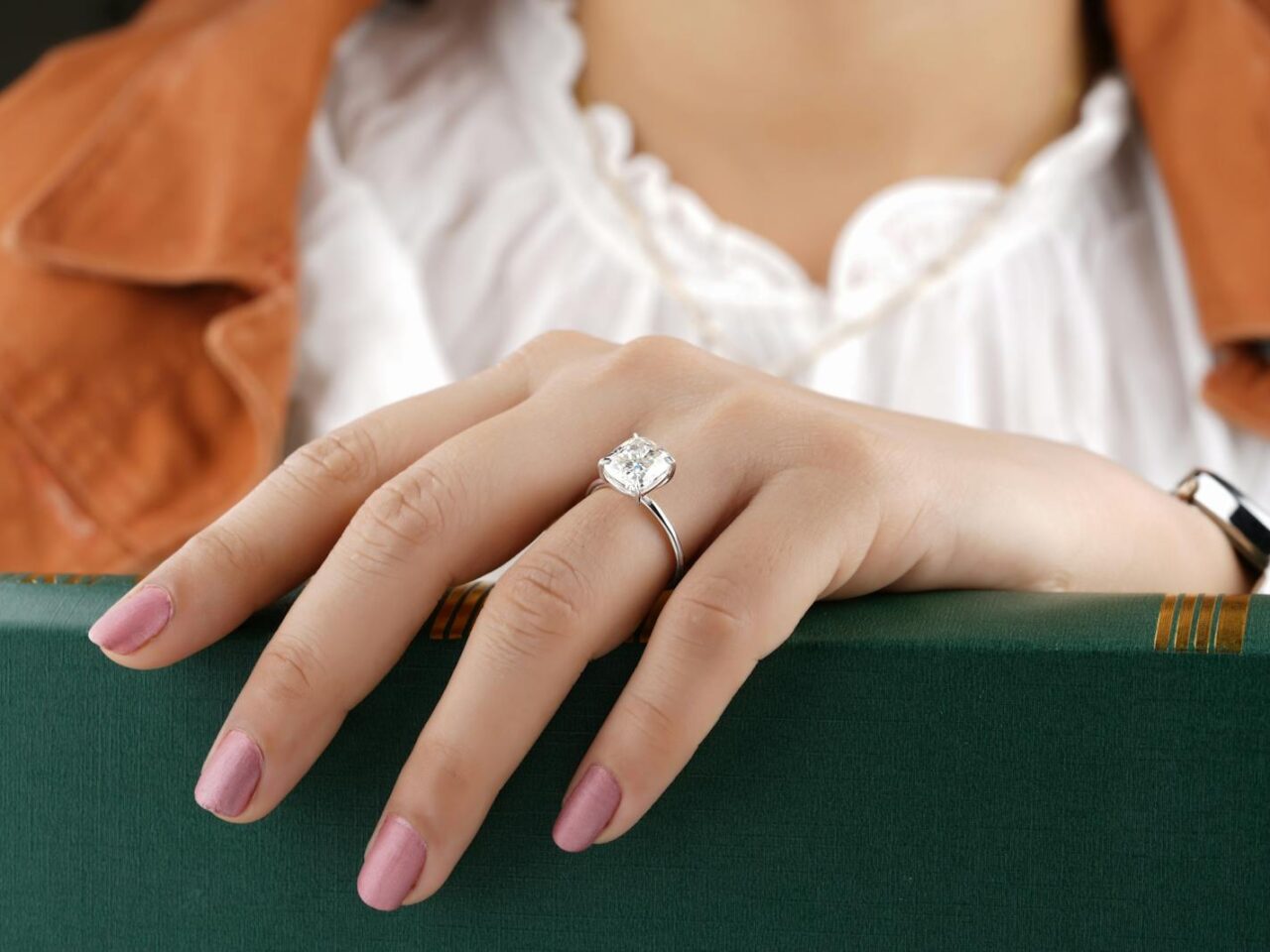 Close-up of a woman's hand with a diamond ring, showcasing fine jewelry against a green book.