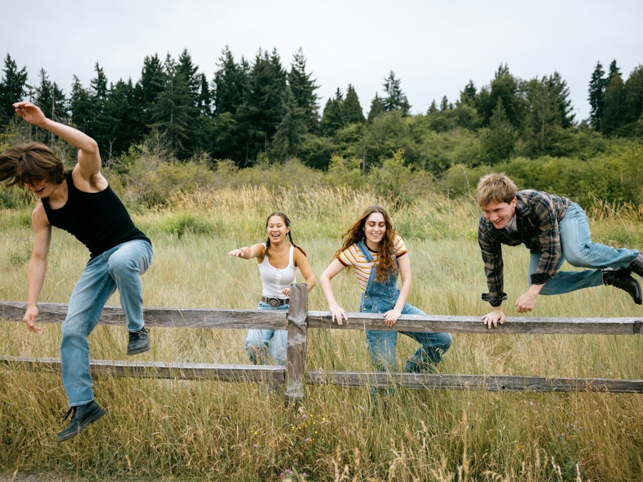 Four friends climbing over a wooden fence outdoors