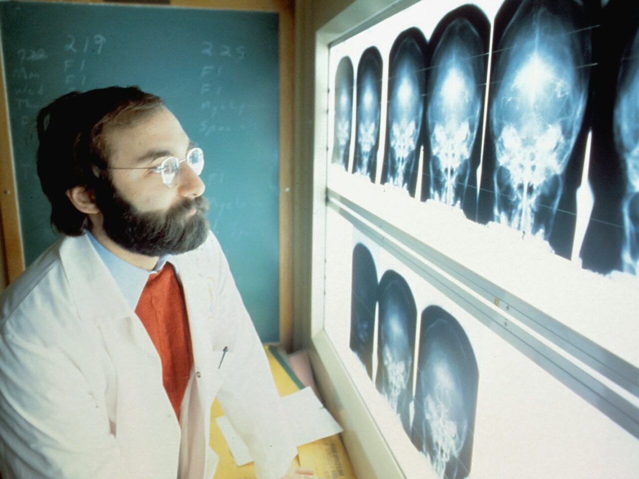 a man in a lab coat and tie looking at an x - ray